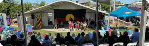 An image of a large crowd of people standing outside in the sunshine watching Darumbal NAIDOC week celebrations.