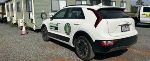 An image of a white Kia Niro Electric SUV parked on gravel outside a green demountable building. This electric vehicle will support the FGP team to meet its Environmental, Social, and Governance (ESG) targets.